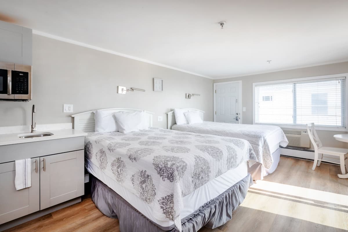 A bedroom with two beds, a white wardrobe, a microwave, and a window with blinds.