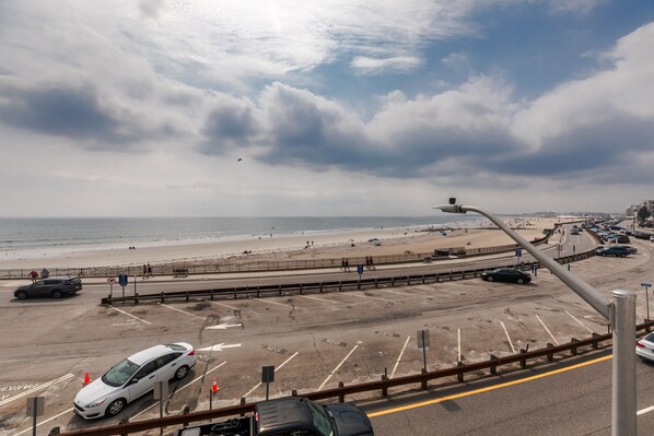 A beachside parking area with cars, a pedestrian walkway, and a view of the beach and ocean. - Atlantic Motel (Hampton)