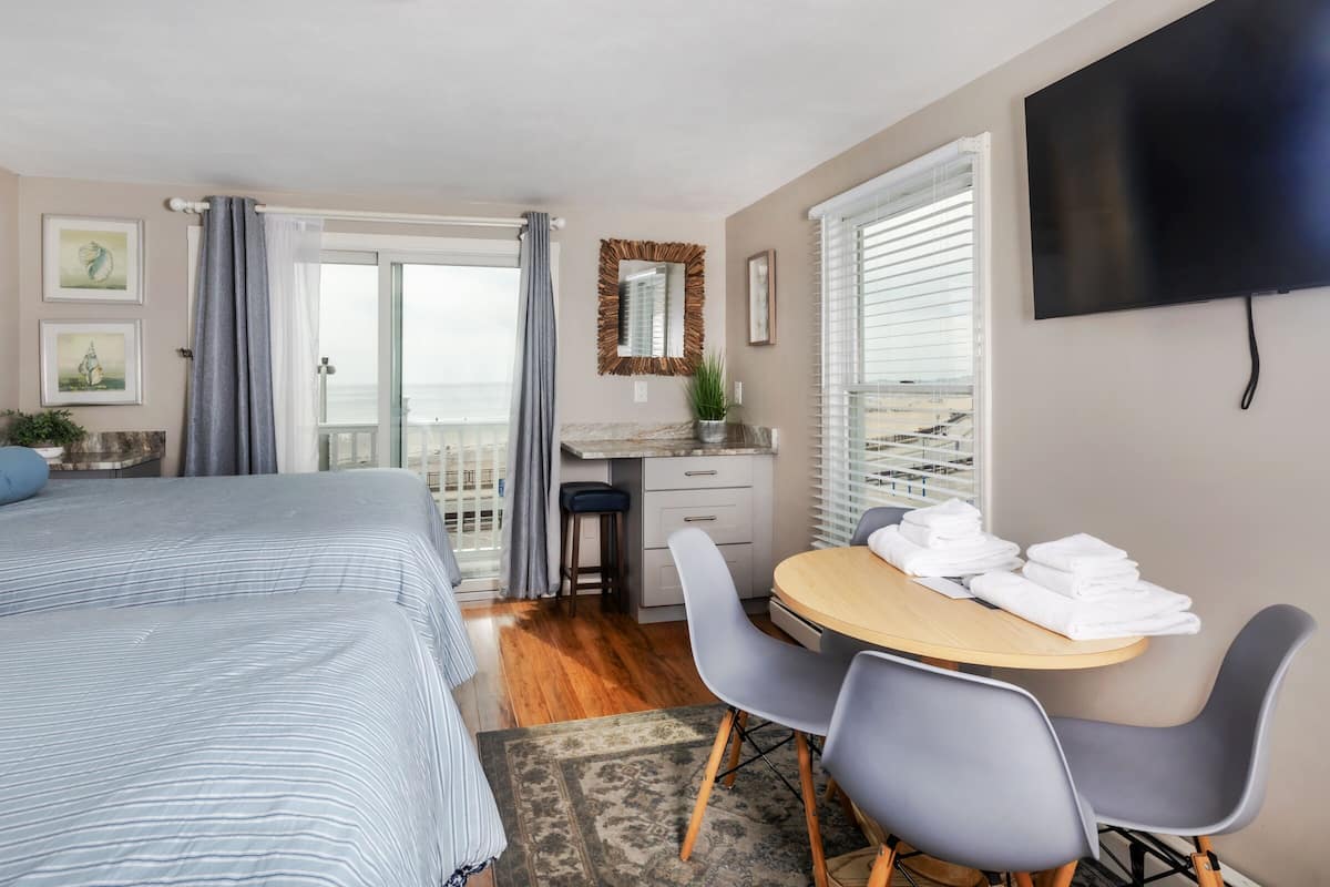 A bedroom with a bed, a desk, a chair, a TV, and a balcony with a view.