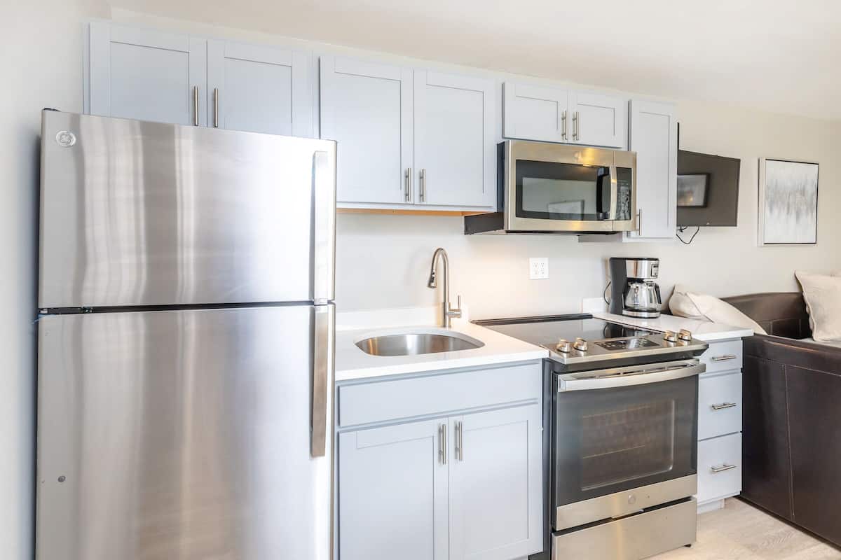 A modern kitchen with light blue cabinets, a stainless steel refrigerator, a microwave, a stove, and a sink.