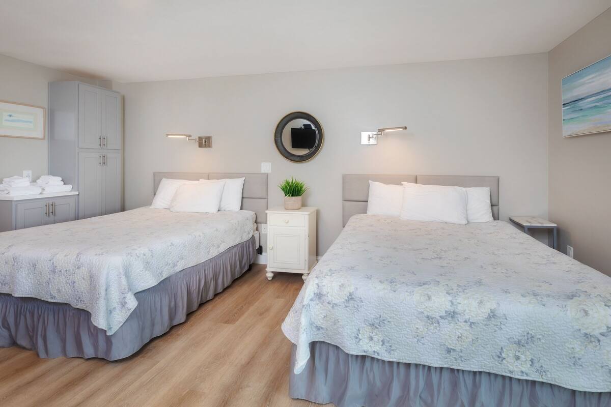 A hotel room with two beds, a wardrobe, a mirror, and a small table with a plant.