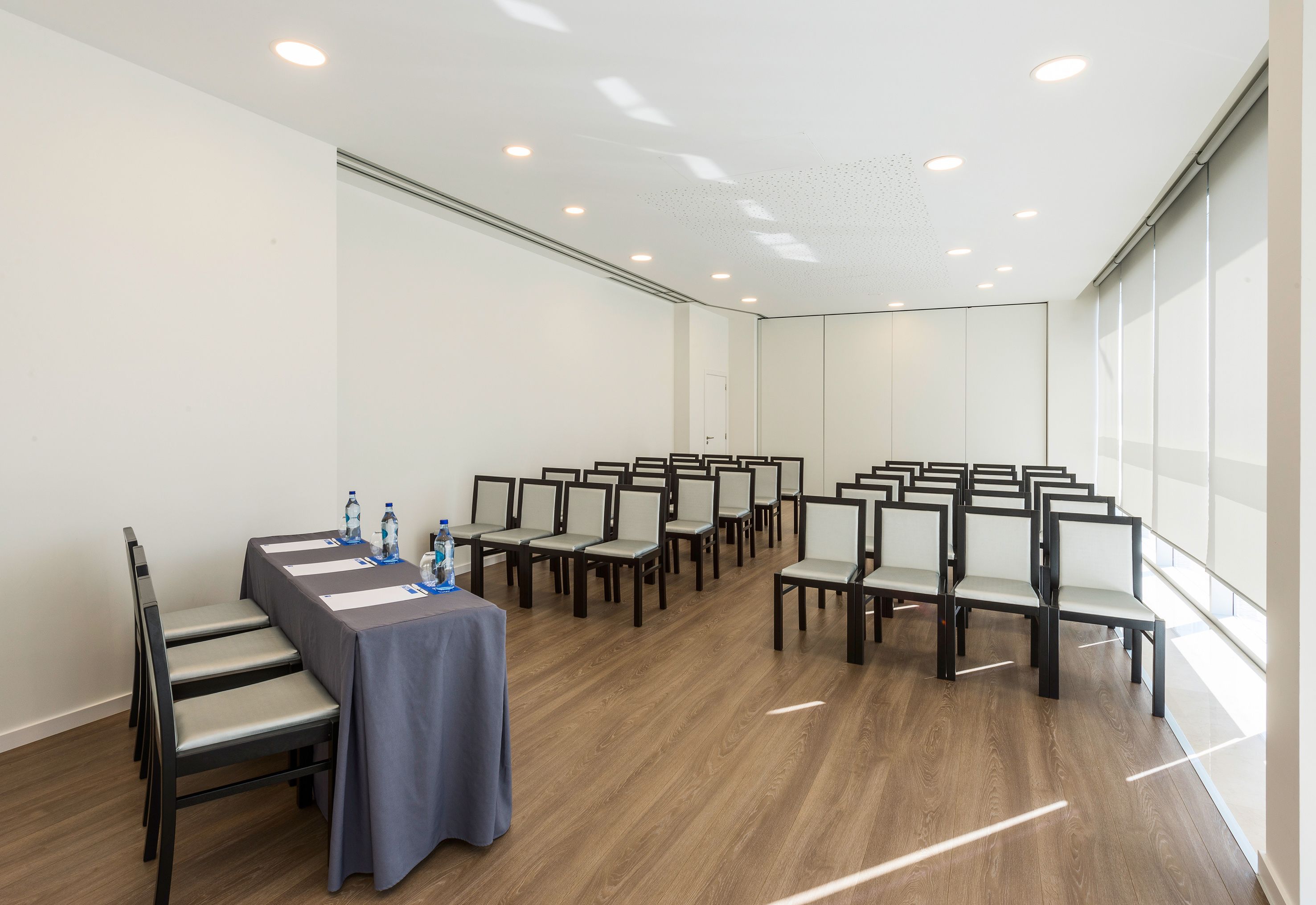 Un salón de conferencias con una larga mesa, sillas y un ventanal.