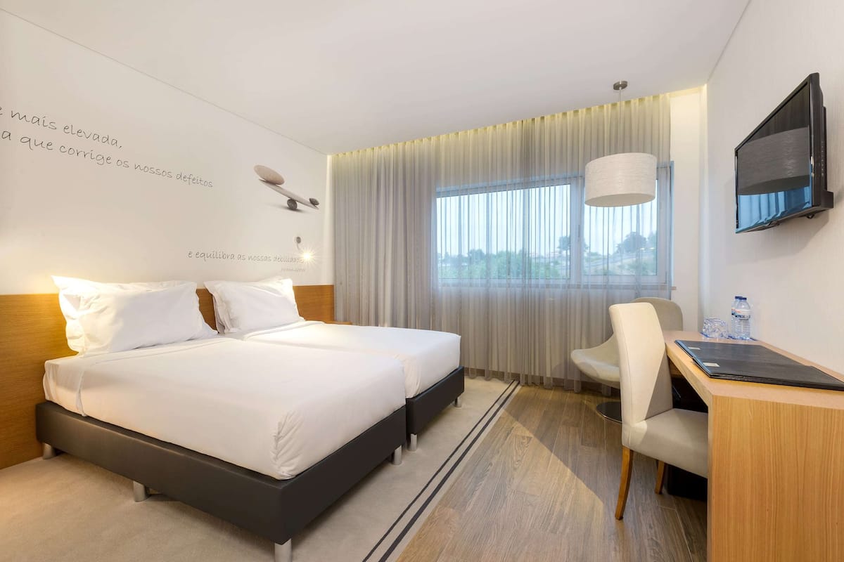 Une chambre d’hôtel avec un grand lit, un bureau, une chaise, une télévision et une fenêtre avec des rideaux.