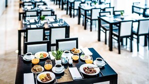 Comedor con varias mesas dispuestas para el desayuno, incluyendo platos de comida, tazas y una planta en maceta.