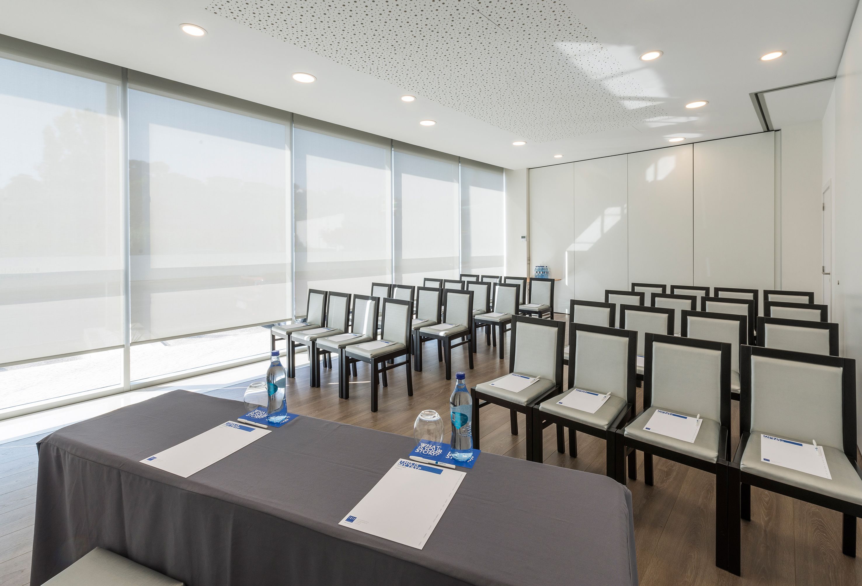 A conference room with rows of chairs, a table with water bottles, and papers.