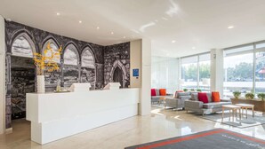 Una moderna zona de recepción con mostrador blanco, un mural de arcos y un área de estar con sofás y una mesa de centro.