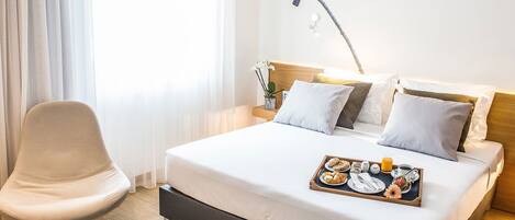 A hotel room with a bed, a chair, and a tray with breakfast items.
