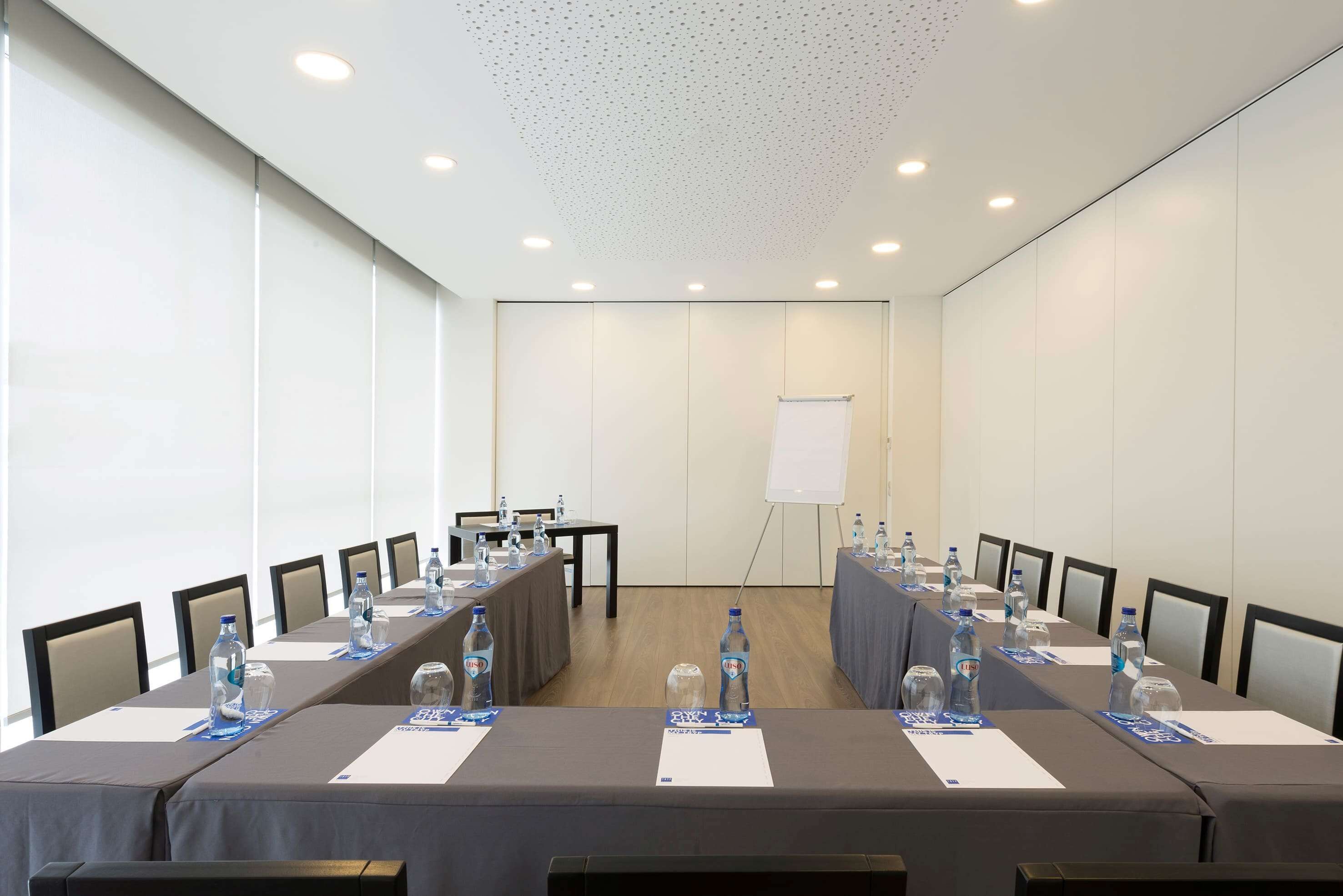 Una sala de conferencias con una larga mesa, sillas, botellas de agua y una pizarra.