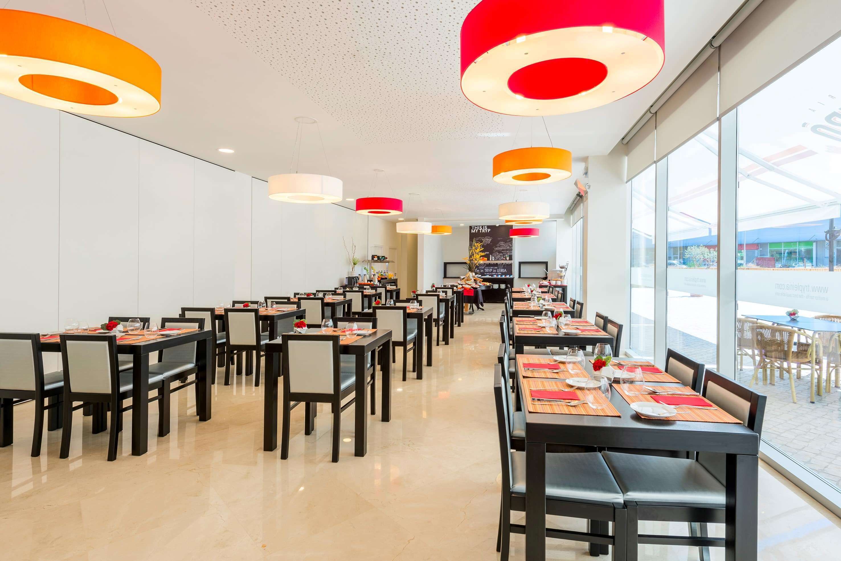 Un espace de restauration moderne, doté de nombreuses tables et chaises, de grandes fenêtres et d’un éclairage lumineux au plafond.