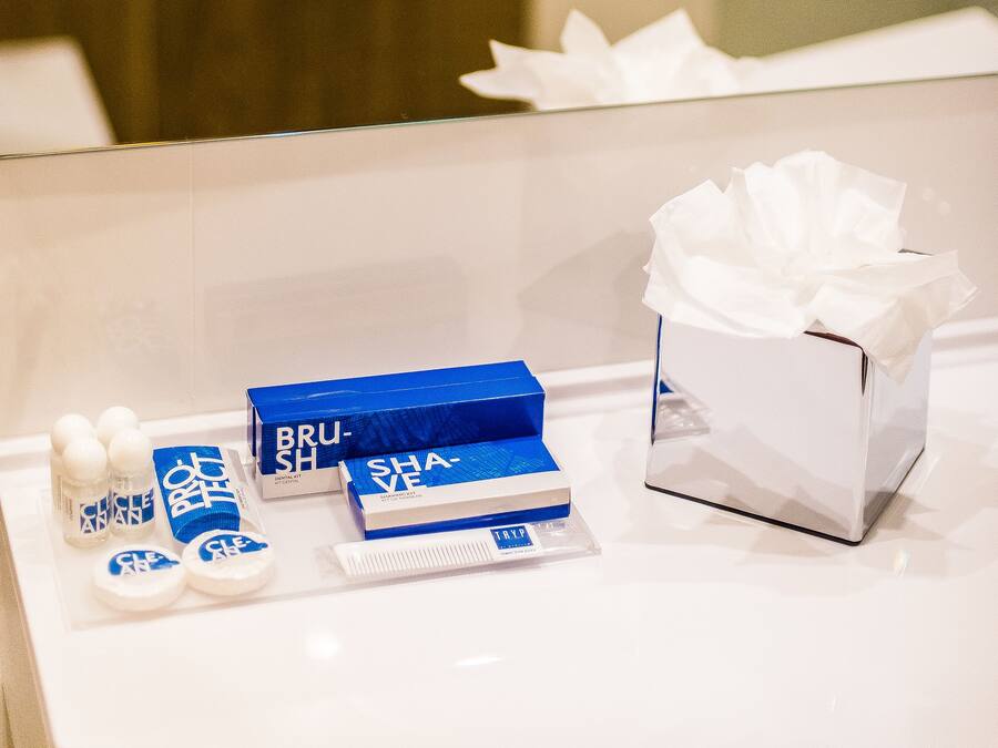 A bathroom counter with toiletries including a blue box labeled 'PROTECT', a white tissue box, and a comb.