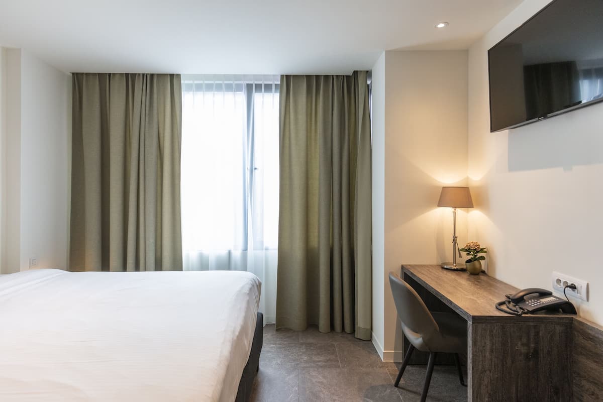 Habitación de hotel con cama, escritorio, silla, lámpara, teléfono y televisión instalada en la pared.