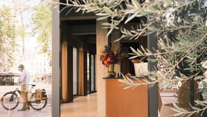 An indoor reception area with a curved reception desk, a large potted plant, and a window overlooking a street with buildings and a bicycle. - The Market by Parkhotel (Kortrijk)