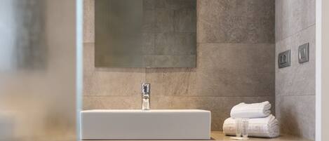 Un baño moderno con un lavamanos rectangular, un espejo grande y un perchero para toallas.