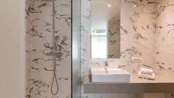 Une salle de bain moderne avec une douche à parois de verre, un pare-baignoire en marbre et un grand miroir au-dessus d’un lavabo blanc.