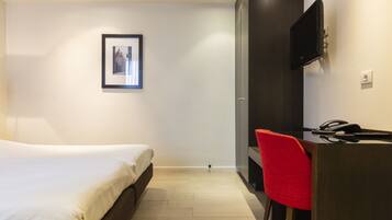 A modern hotel room with a bed, a desk with a chair, a mounted TV, and a framed picture on the wall.