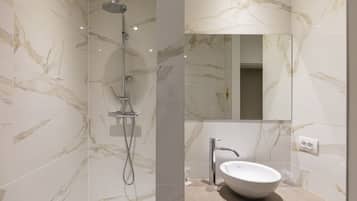 Un baño moderno con paredes de mármol, ducha y lavamanos con espejo.