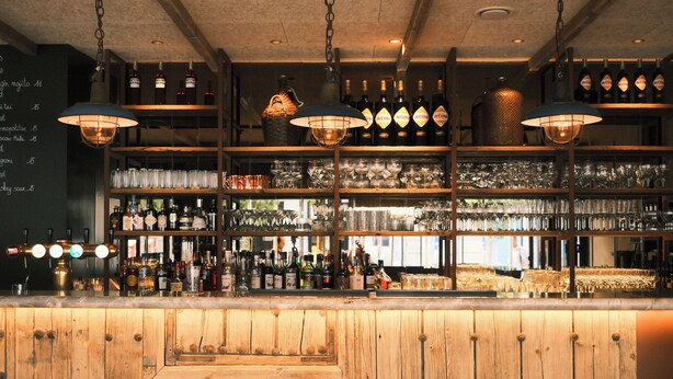 A bar with wooden stools, shelves of bottles, and hanging lights. - The Market by Parkhotel (Kortrijk)