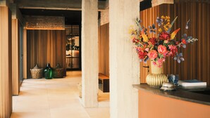 A hotel lobby with a reception desk, a large floral arrangement, and a wooden bench. - The Market by Parkhotel (Kortrijk)