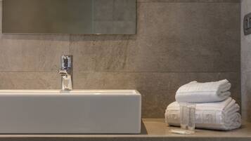 A bathroom with a white sink, a mirror, and a stack of white towels.