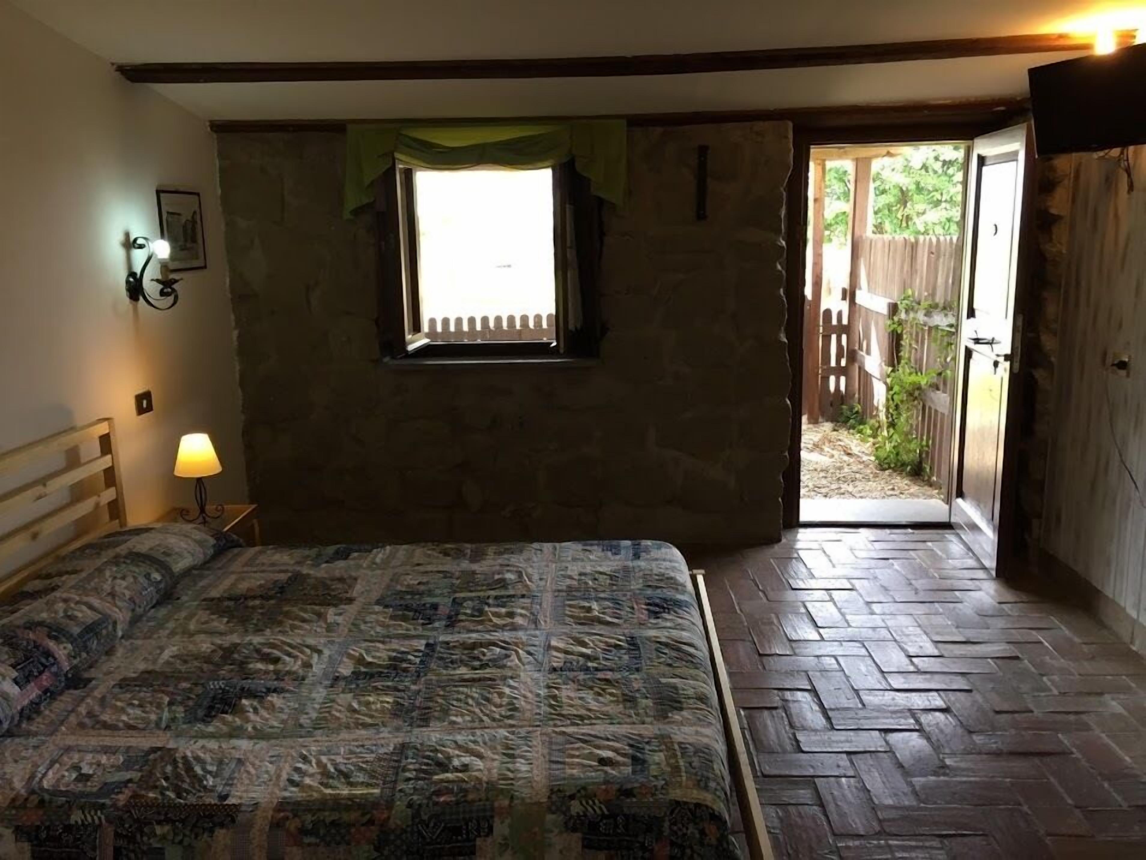 Un dormitorio con cama, ventana, puerta que da al exterior y una mesita con lámpara.
