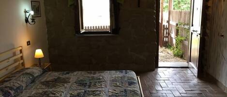 Un dormitorio con cama, ventana, puerta que da al exterior y una mesita con lámpara.