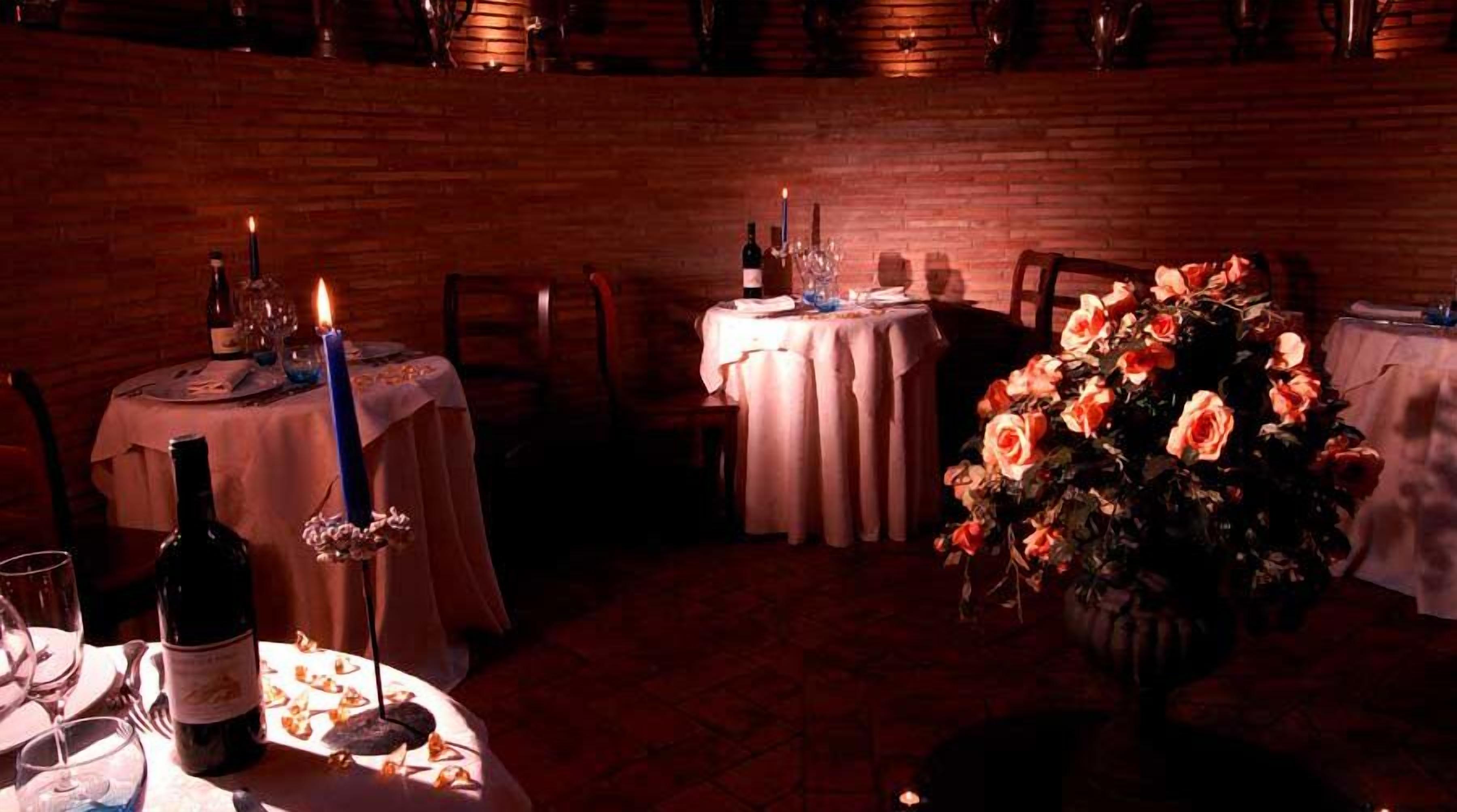 A dimly lit restaurant with wooden walls, tables set with candles, wine bottles, and a large floral centerpiece.