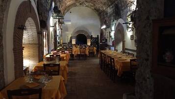 Un étroit couloir voûté en pierre, agrémenté de tables et de chaises, laisse supposer qu’il s’agit d’un restaurant ou d’un espace de restauration situé dans un bâtiment historique.