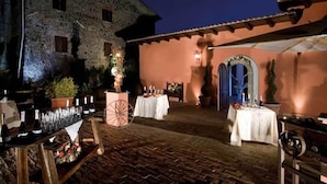 An outdoor dining area with tables set for a meal, a large stone building in the background, and a rustic wooden fence. - Agriturismo Monte Due Torri (Genzano di Roma)