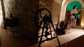 A stone-walled room with a vintage mechanical device, a chair, and a table with flowers. - Agriturismo Monte Due Torri (Genzano di Roma)