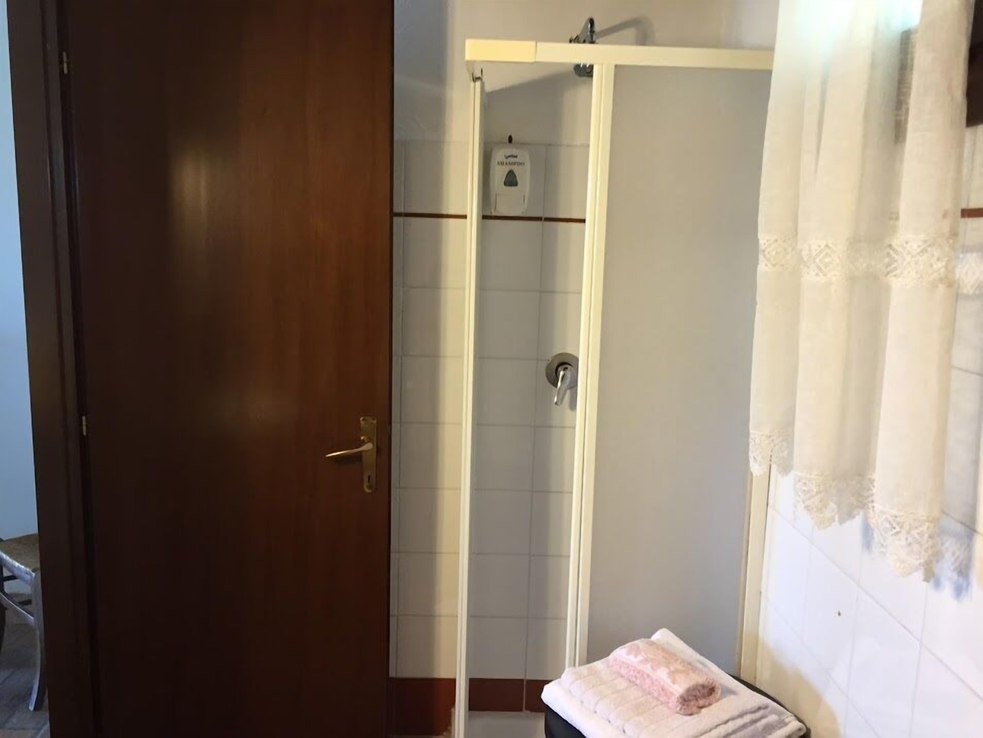 Un baño con puerta de madera, zona de ducha y toalla en un perchero.