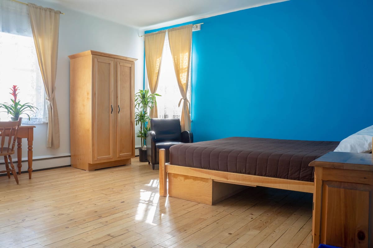 Una habitación con cama, escritorio, silla, armario y dos plantas en macetas.