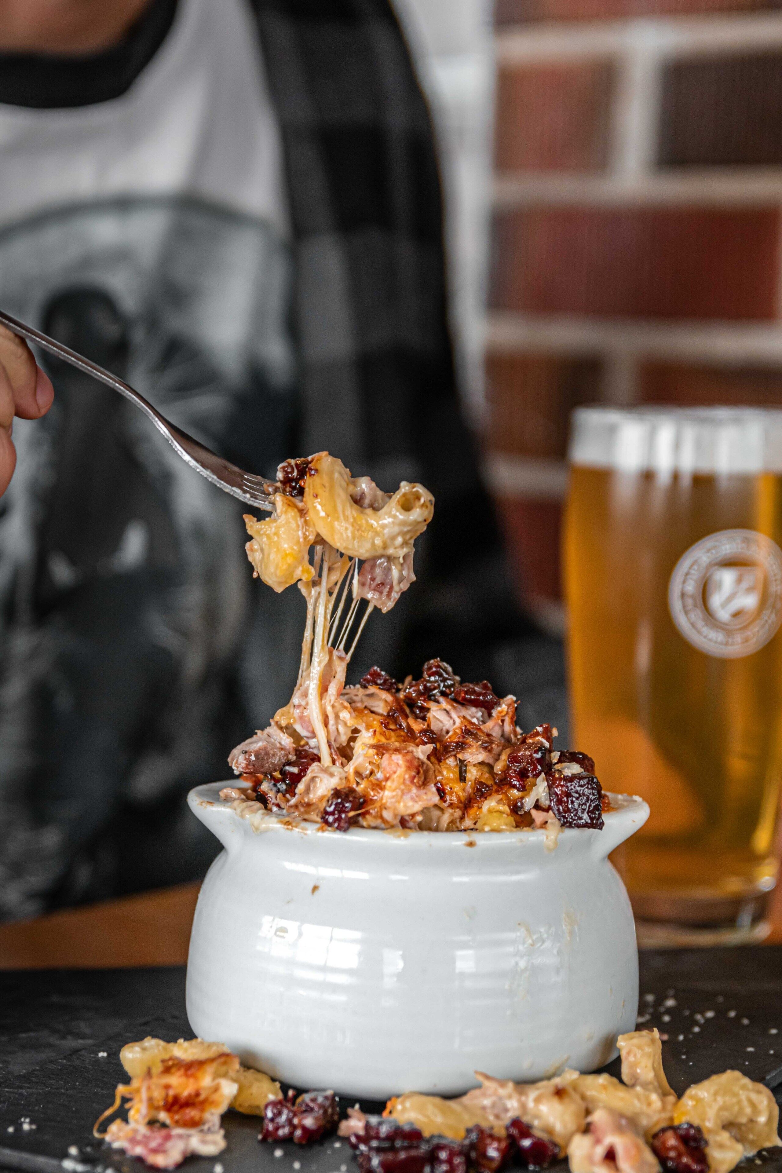 A white ceramic bowl filled with a dessert, a fork lifting a piece, and a glass of beer in the background.