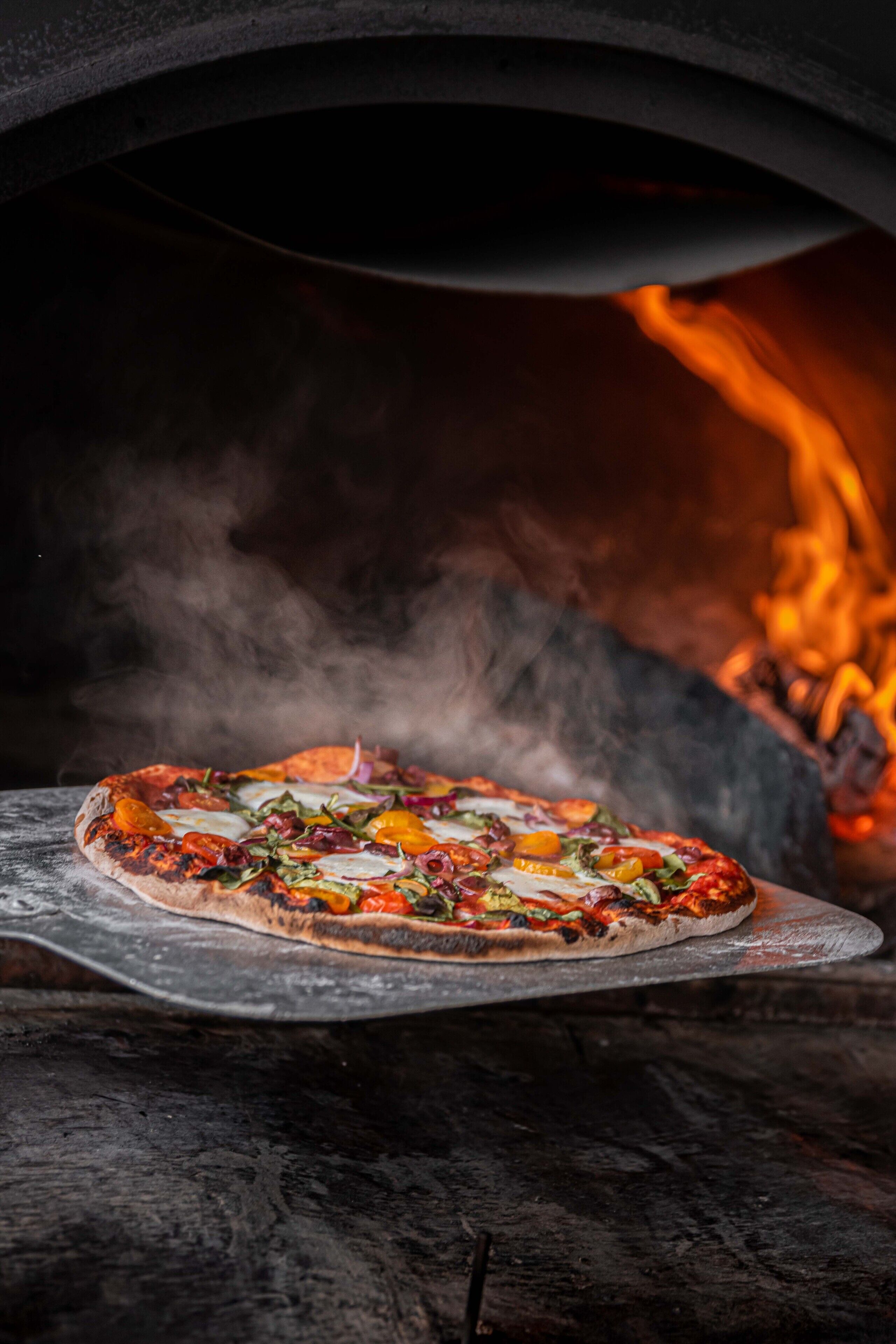 Una pizza dentro de un horno de leña con llamas visibles.