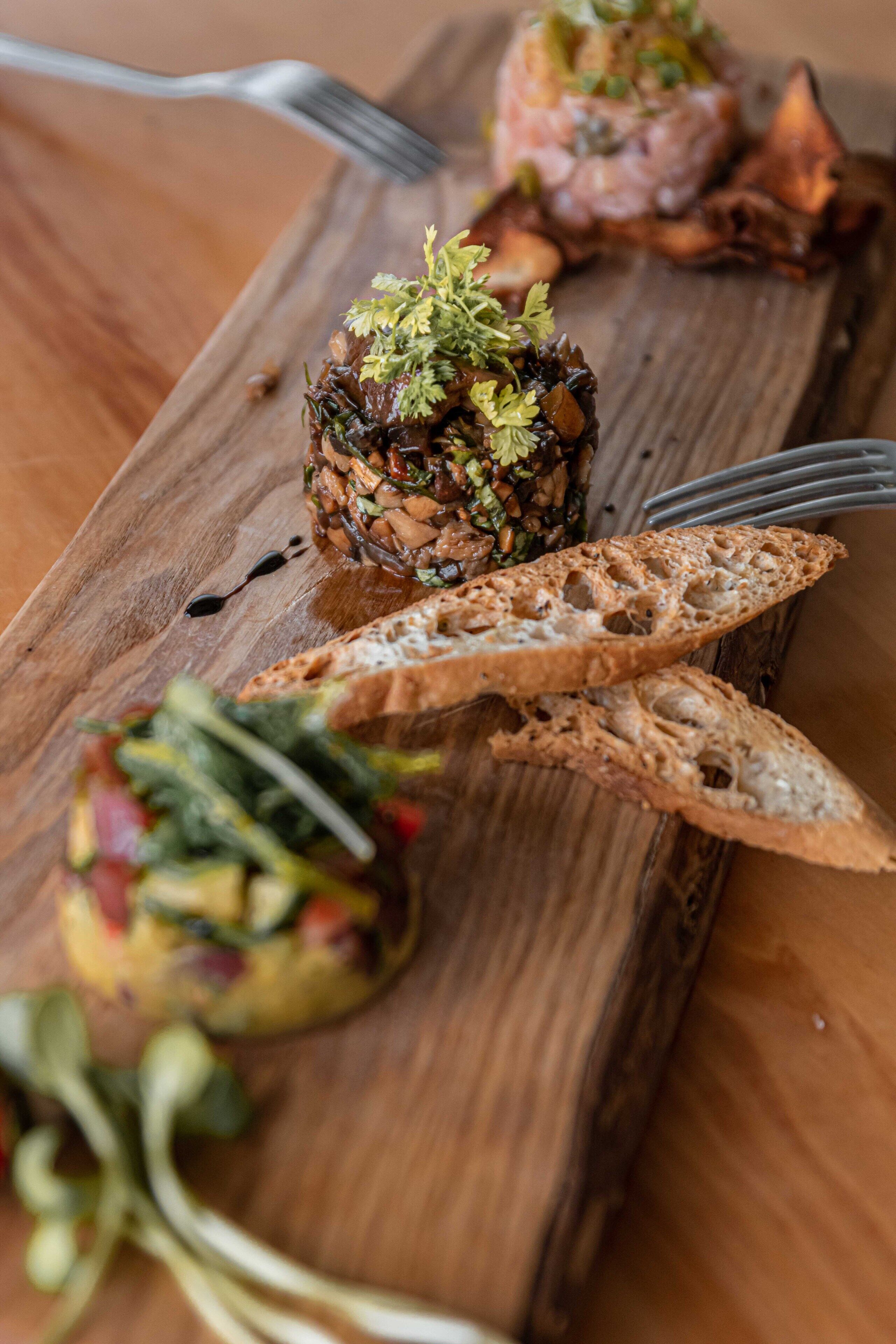 Une planche en bois sur laquelle sont disposés divers plats, notamment une salade et un plat de viande, ainsi que deux morceaux de pain.