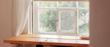 A wooden table with a window above it, two wooden stools, and a bicycle in the background.