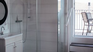 Un baño moderno con ducha envuelta en vidrio, lavamanos blanco y cama grande.