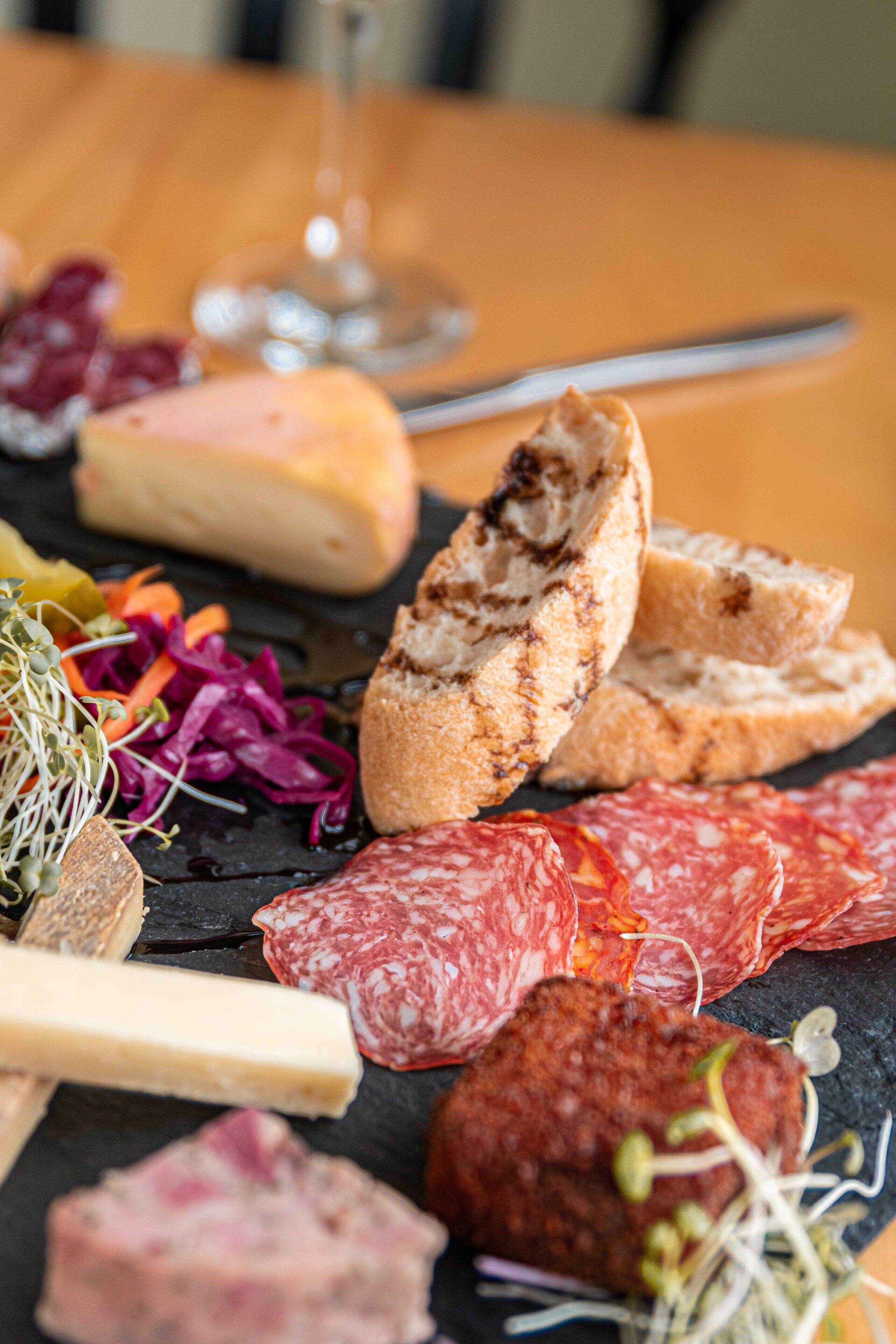 A charcuterie board with various meats, cheeses, and vegetables on a slate board.