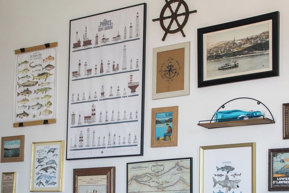 Un dormitorio con cabecera de madera, cama con ropa de cama blanca y azul, y varias obras de arte náuticas enmarcadas en la pared.