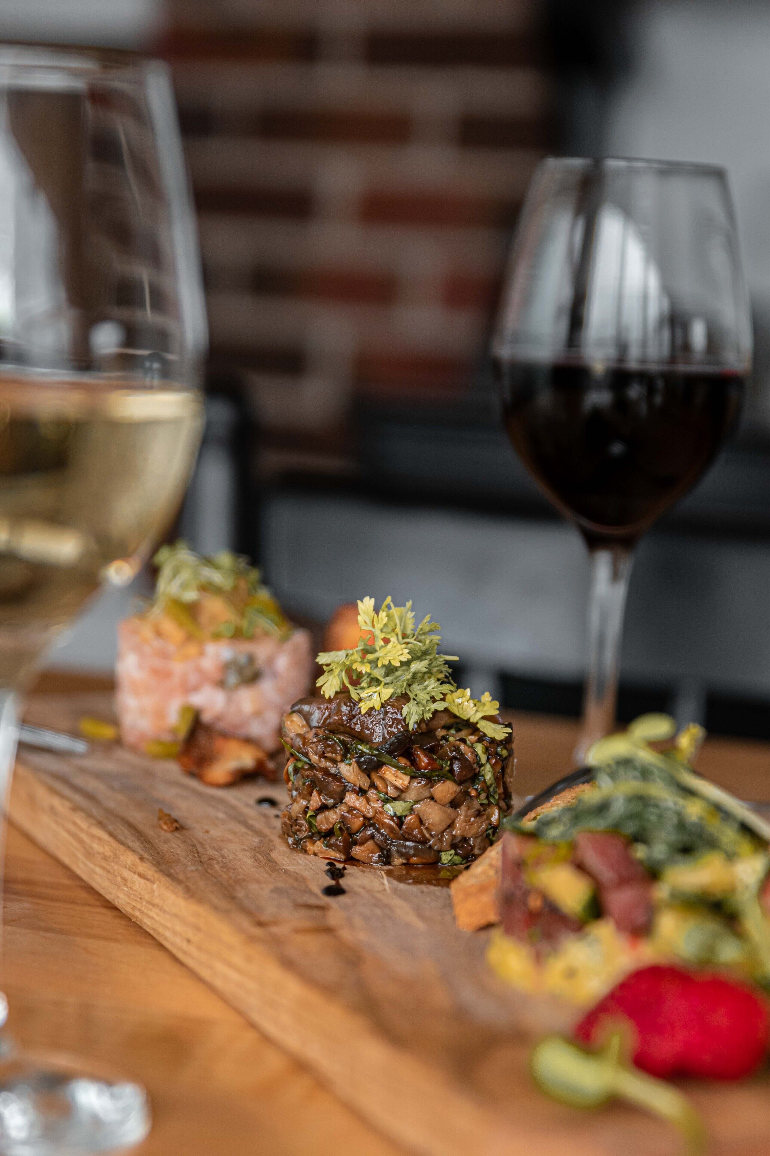 A wooden table with a dish of food garnished with herbs, a glass of white wine, and a glass of red wine.