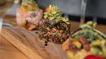 A wooden table with a dish of food garnished with herbs, a glass of white wine, and a glass of red wine.