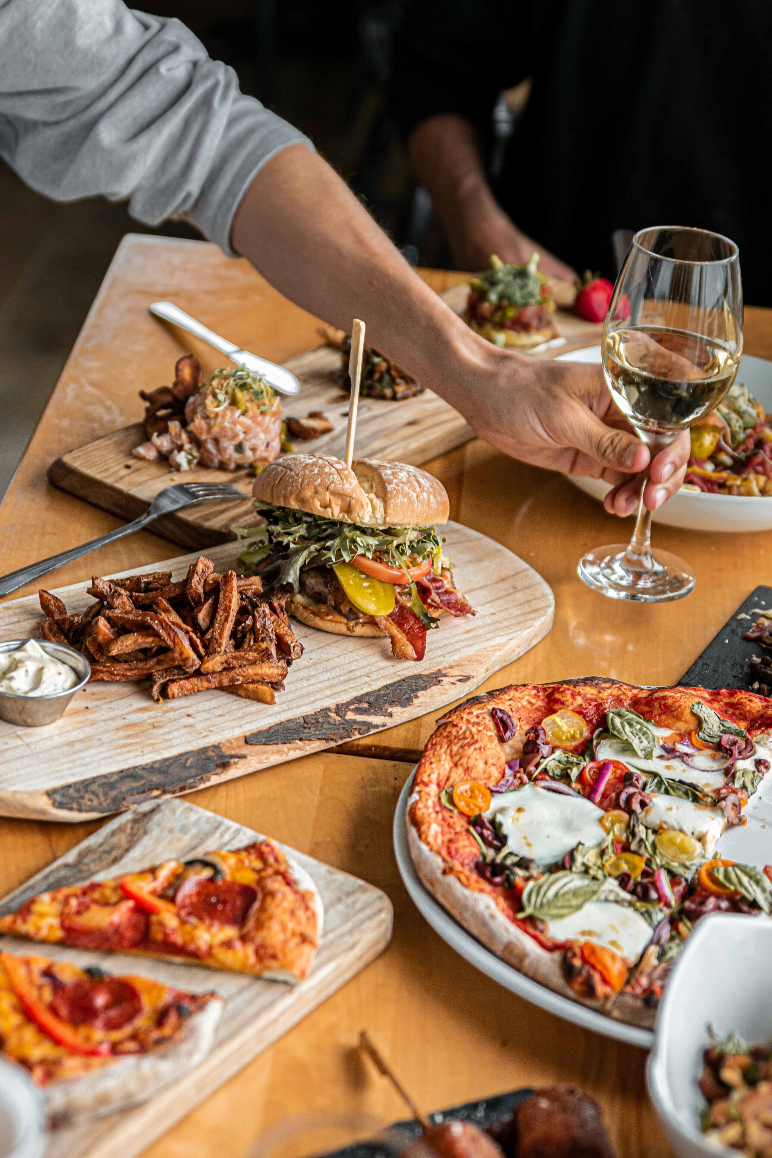 Ein Esstisch mit verschiedenen Speisen, darunter Burger, Pommes und Pizza.