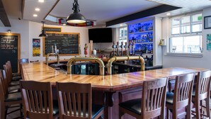Una zona de bar con mostrador de madera, varios taburetes, un menú en una pizarra y un televisor fijado a la pared.