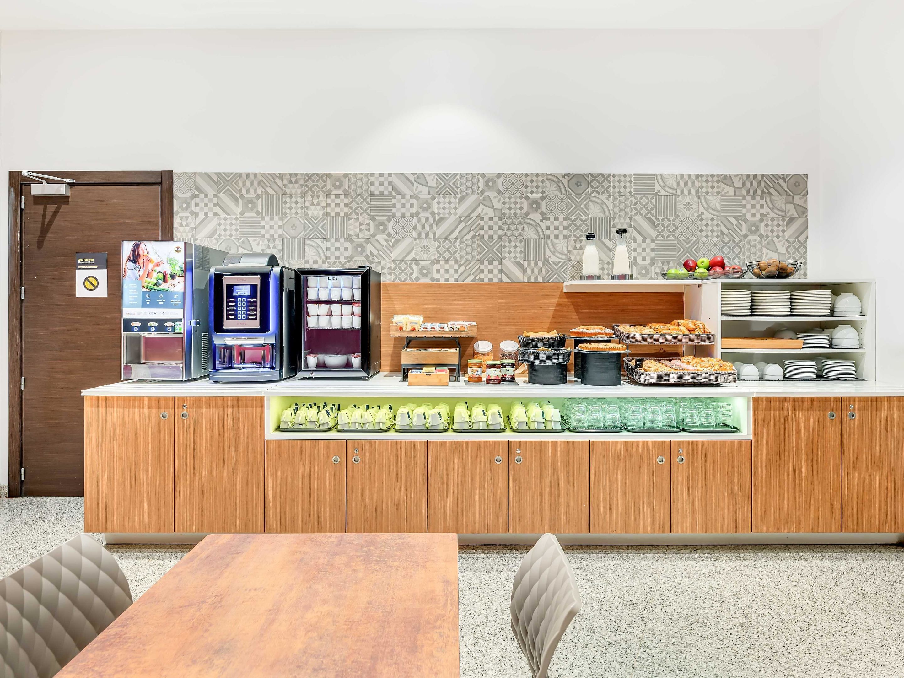A modern kitchenette with a coffee machine, tea maker, and various food items.