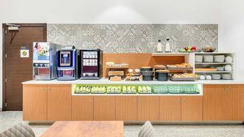 A modern kitchenette with a coffee machine, tea maker, and various food items.