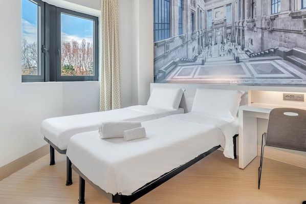 Habitación de hotel con dos camas, un ventanal grande, cortina, escritorio y una silla.
