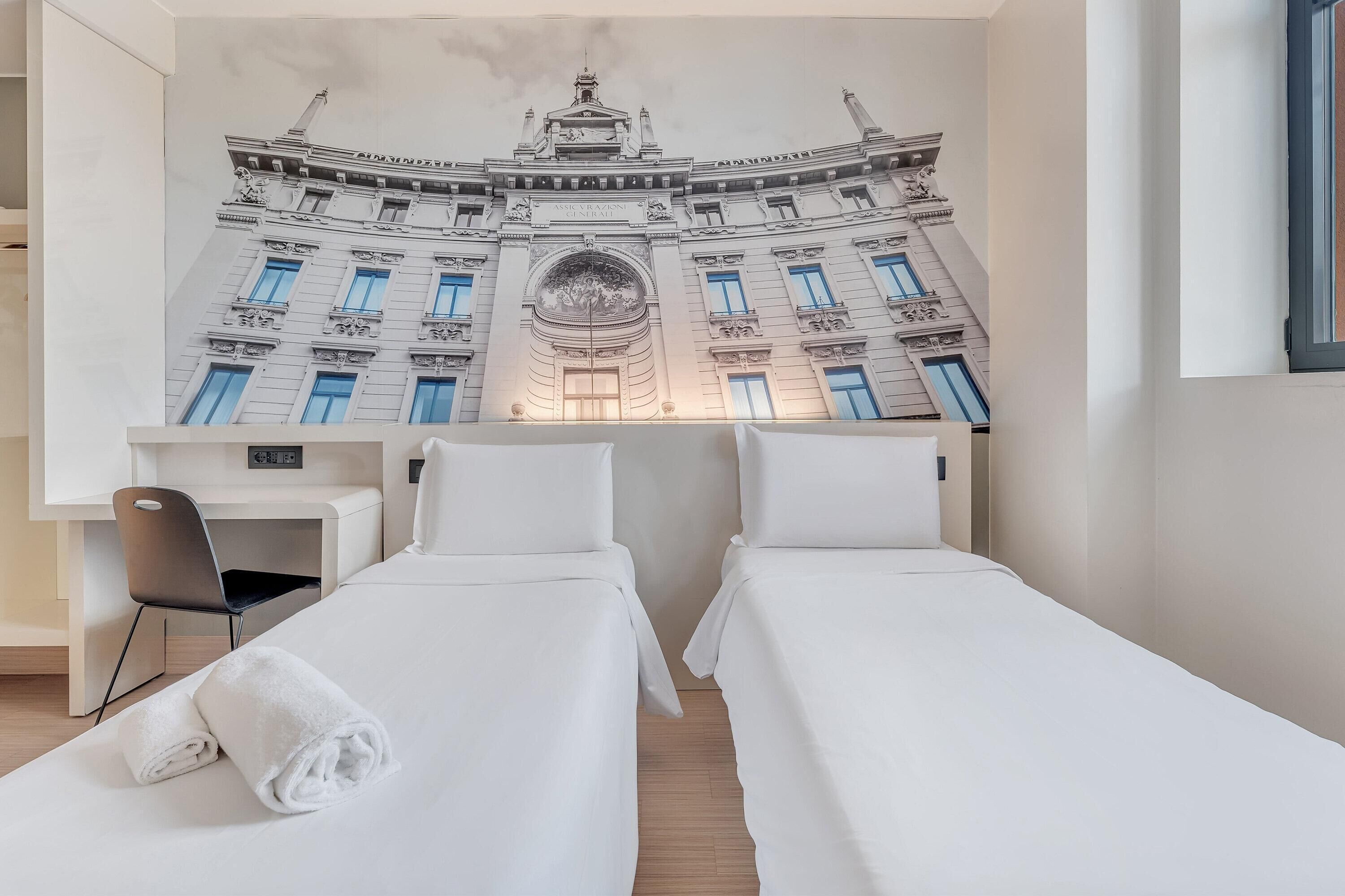 A hotel room with two beds, a desk, and a chair.