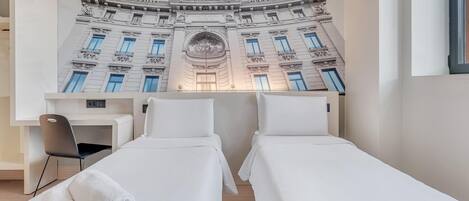 A hotel room with two beds, a desk, and a chair.
