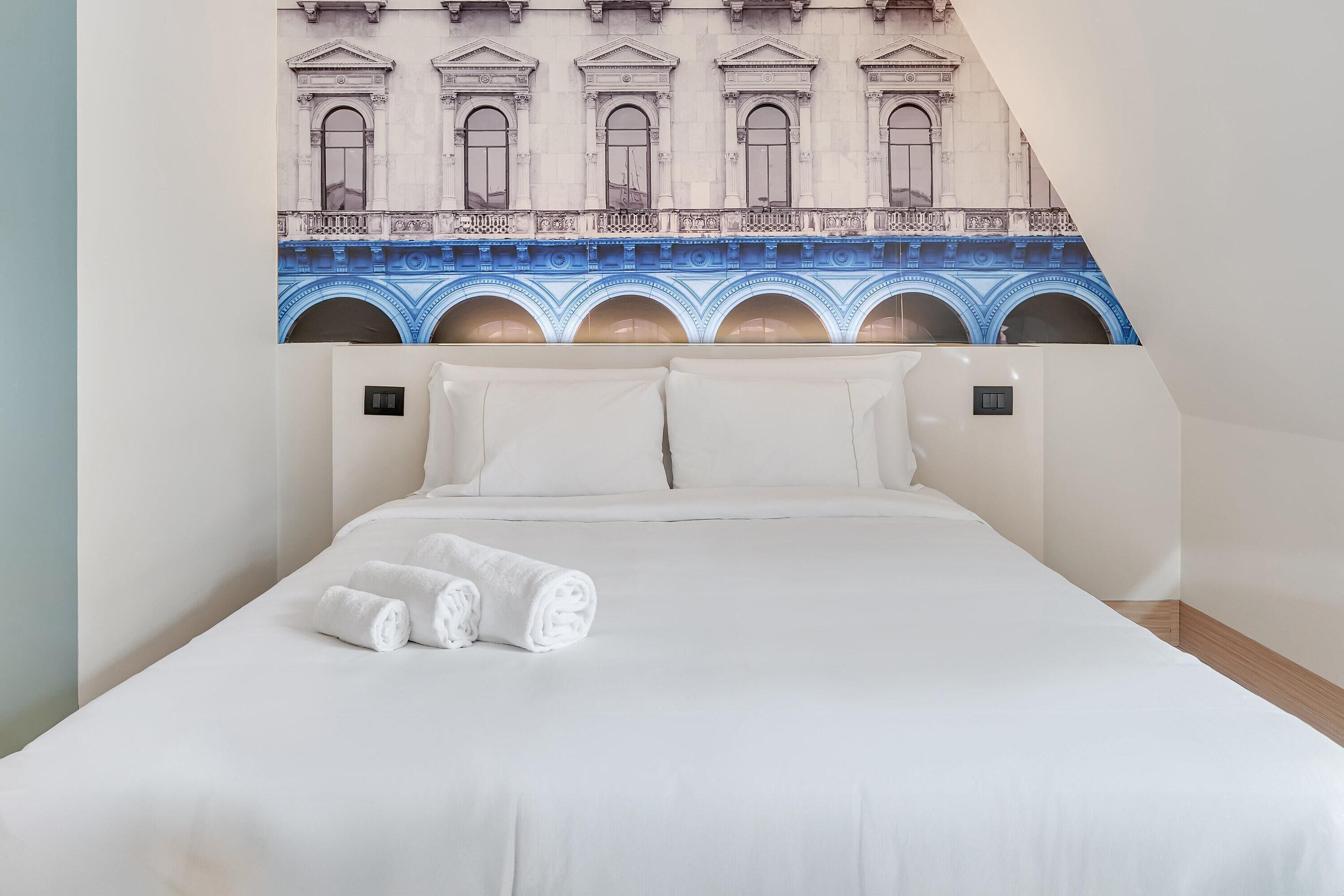 Una camera d'albergo con un letto grande, due cuscini e due asciugamani arrotolati.