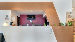 A reception desk with a modern design, featuring a wooden accent wall, a flat-screen TV, and a digital information board. - B&B Hotel Milano San Siro (Milan)