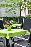Una mesa con mantel verde, rodeada de sillas con cojines negros y una planta en maceta con flores rojas.